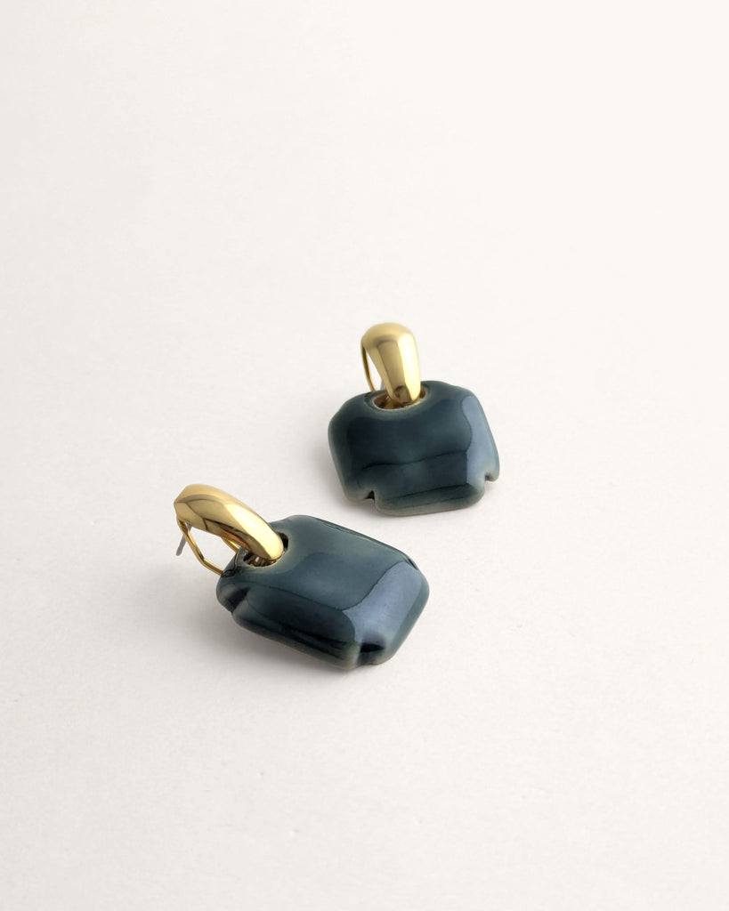 Paire de boucles d’oreilles forme carré arrondi coloris vert céladon, inspiration vintage année 80, au volume géométrique adouci, finition émaillée, montées sur un élément plaqué or.  Bijou contemporain fait main, style minimal et intemporel par Lydie Smith artisan bijoutier et céramiste basée à Paris.