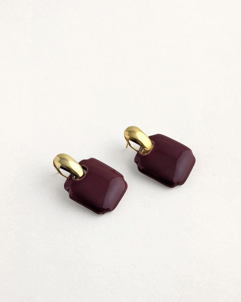 Paire de boucles d’oreilles forme carré arrondi en bordeaux, inspiration vintage année 80, au volume géométrique adouci, finition émaillée, montées sur un élément plaqué or.  Bijou contemporain fait main, style minimal et intemporel par Lydie Smith artisan bijoutier et céramiste basée à Paris.