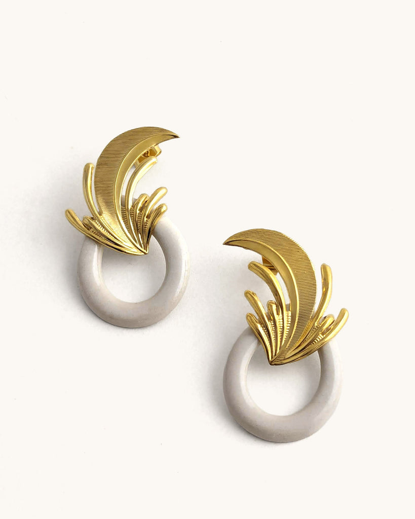 Boucles d’oreilles art déco blanc crème et dorées, ornées d’un motif végétal sculpté rappelant l’élégance des années Gatsby, avec un anneau noir laqué contrastant. Créé par LYDIE SMITH artisan céramiste et bijoutier dans son atelier à Asnières en France
