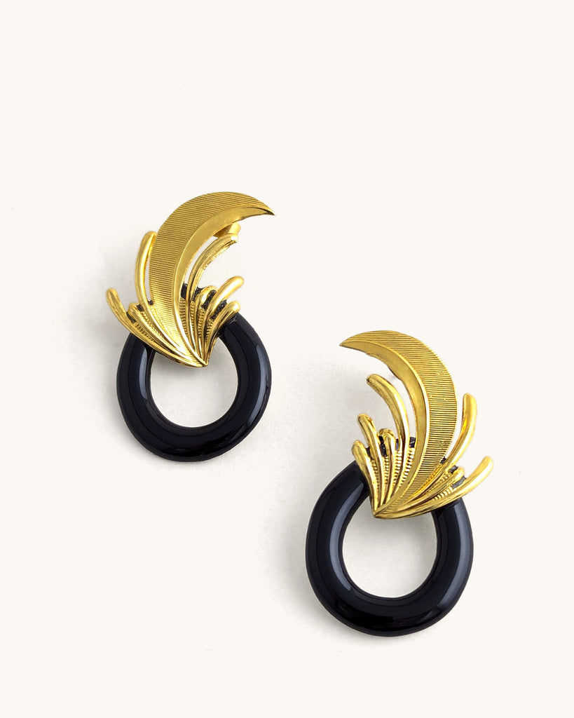 Boucles d’oreilles art déco noires et dorées, ornées d’un motif plume sculpté rappelant l’élégance des années Gatsby, avec un anneau noir laqué contrastant. Créé par LYDIE SMITH artisan céramiste et bijoutier dans son atelier à Asnières en France