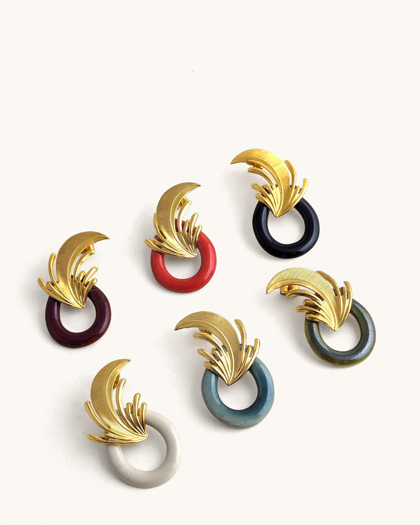 Boucles d’oreilles art déco, existent en plusieurs coloris : blanc crème, rouge, bordeaux, vert céladon et vert kaki. plaqué or et ornées d’un motif de feuille sculpté rappelant l’élégance des années Gatsby, avec un anneau noir laqué contrastant. Créé par LYDIE SMITH artisan céramiste et bijoutier dans son atelier à Asnières en France